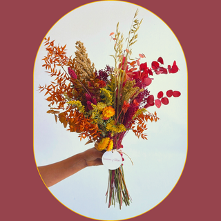 a bouquet of seasonal dried flowers in vibrant red, orange and golden yellow, held up by a person's hand against a white wall