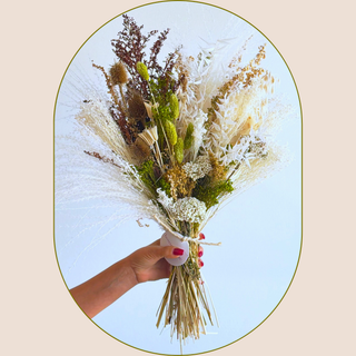 a bouquet of seasonal dried flowers in cream, chocolate brown and olive green, held up by a person's hand against a white wall